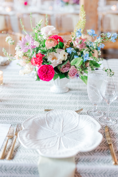 A table setting with white china, gold flatware, crystal stemware, and vibrant florals.