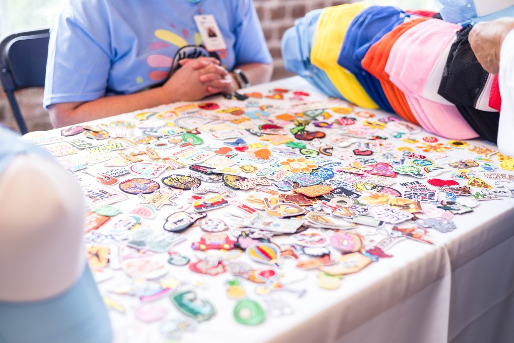 Iron-on patches and trucker hats cover a table at the Power House event venue. A volunteer is ready to assist.
