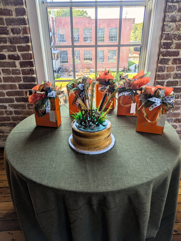 A hunting-themed groom's cake sits on a table with blaze orange goody bags.