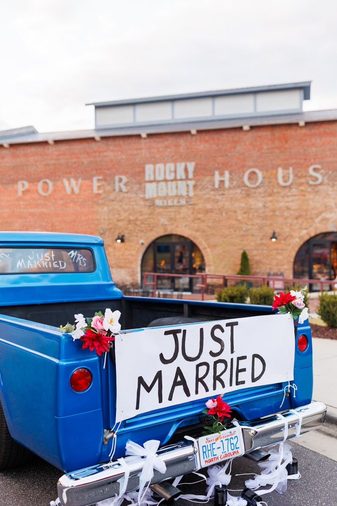 A blue pickup truck sits outside of the Power House at Rocky Mount Mills. The pickup truck has flowers and a Just Married sign on the back.