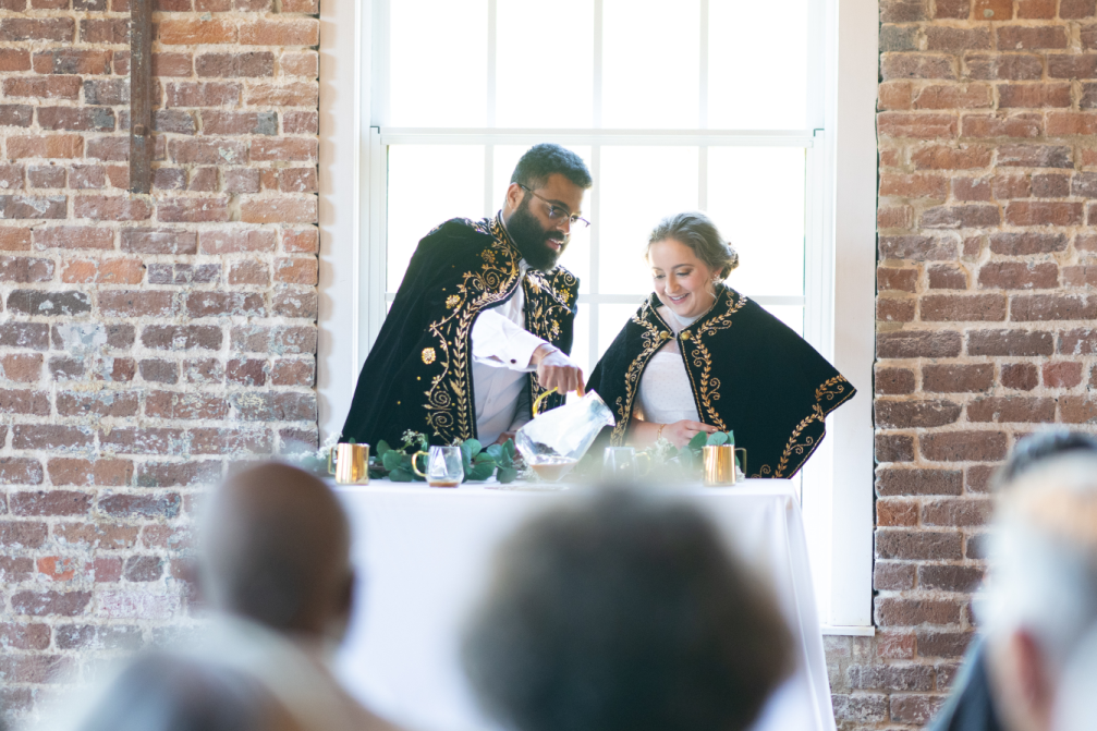 A groom pours coffee while his bride, in traditional Ethiopian kabas, watches, as a part of their wedding ceremony in the River Overlook at Rocky Mount Mills.